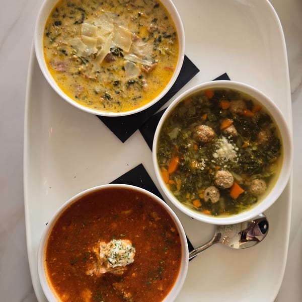 Three bowls of soup on a white platter: creamy yellow, green with meatballs, and red with a dollop of cream.