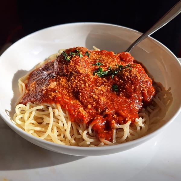 Spaghetti with meatballs, red sauce, parmesan cheese, and parsley in a white bowl.