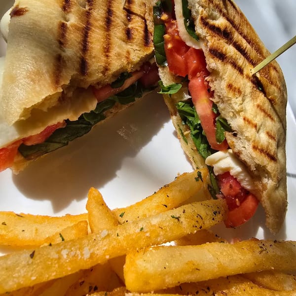 Grilled panini sandwich with tomatoes, mozzarella, and basil, served with seasoned french fries.