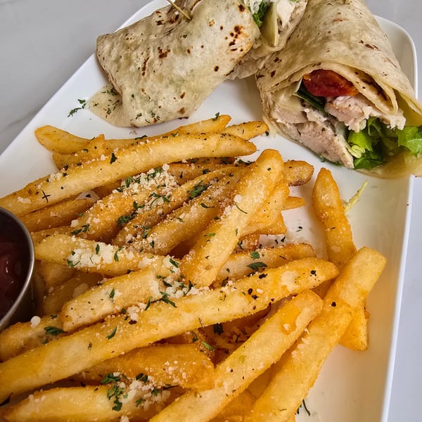 Two chicken wraps with lettuce, tomatoes, and cheese, served with a side of seasoned french fries.