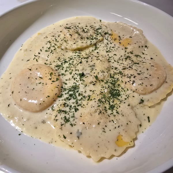Ravioli pasta in a creamy white sauce, garnished with parsley and grated cheese.
