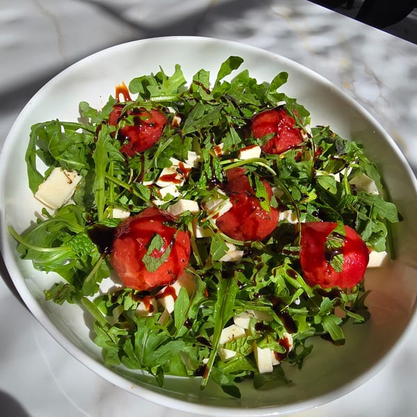 Arugula salad with watermelon, feta cheese, mint, and balsamic glaze in a white bowl.